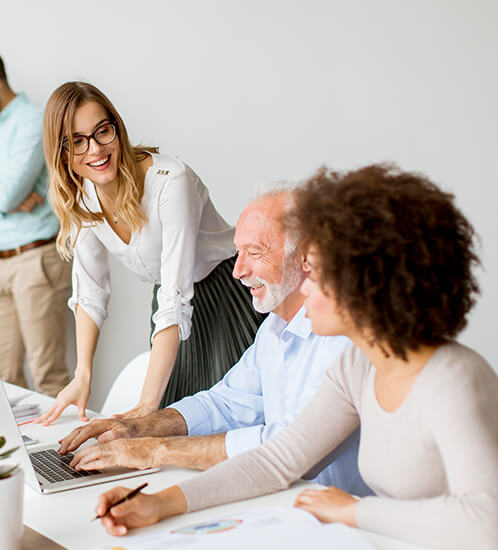 Group of colleagues smiling and discussing work around a table with a laptop.