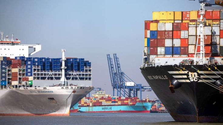 Multiple container ships docked at port with cranes loading cargo. Title: International Cargo Ships at Port Terminal